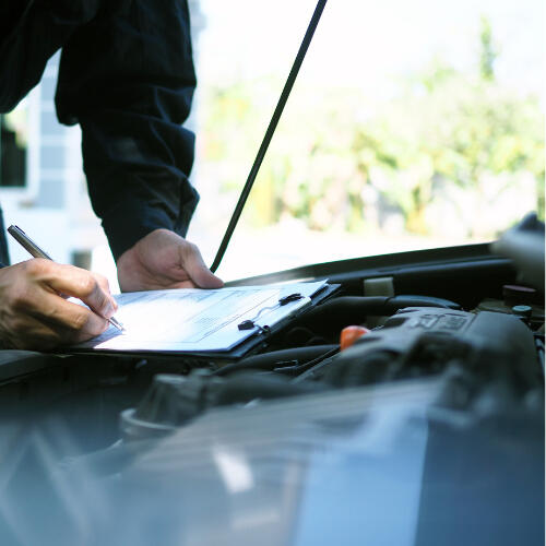 A mechanic notes findings on a clipboard while inspecting a car’s engine bay, symbolising Maxamy’s thorough mobile diagnostics and vehicle inspections.
