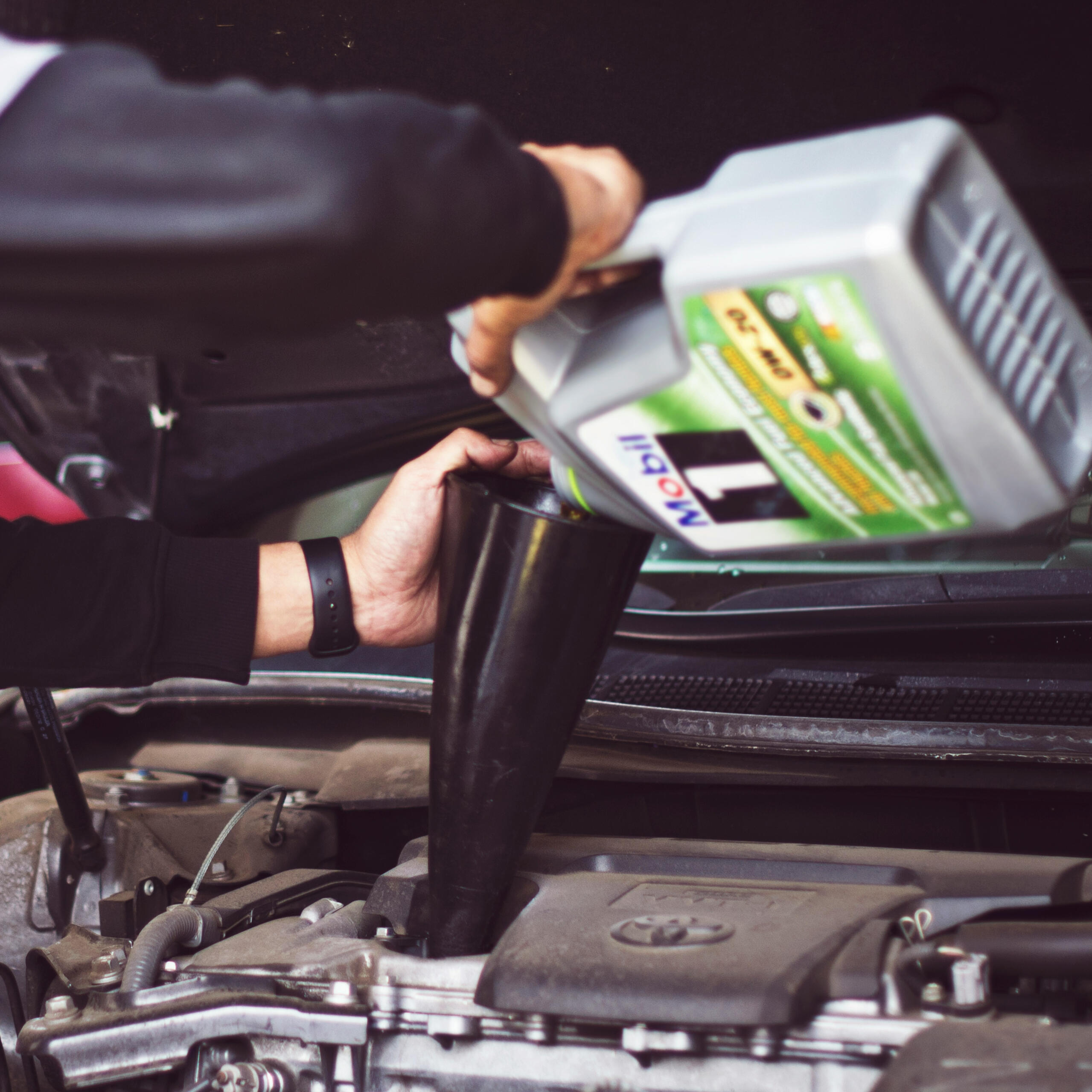 Close‑up of a mechanic pouring fresh engine oil into a car using a funnel, illustrating Maxamy’s mobile servicing and maintenance across Berkshire.