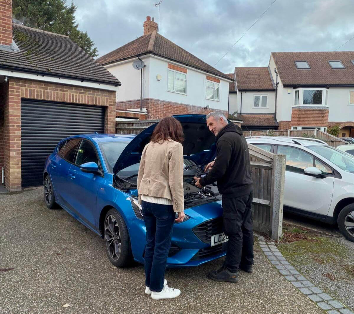 Carrying out a mobile diagnostic scan Maxamy mobile mechanic running a diagnostic scan on a blue car while explaining the results to the vehicle owner on her driveway.