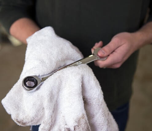 Mechanic wiping down a ratchet tool with a cloth after completing a mobile car service, showcasing attention to detail and cleanliness.